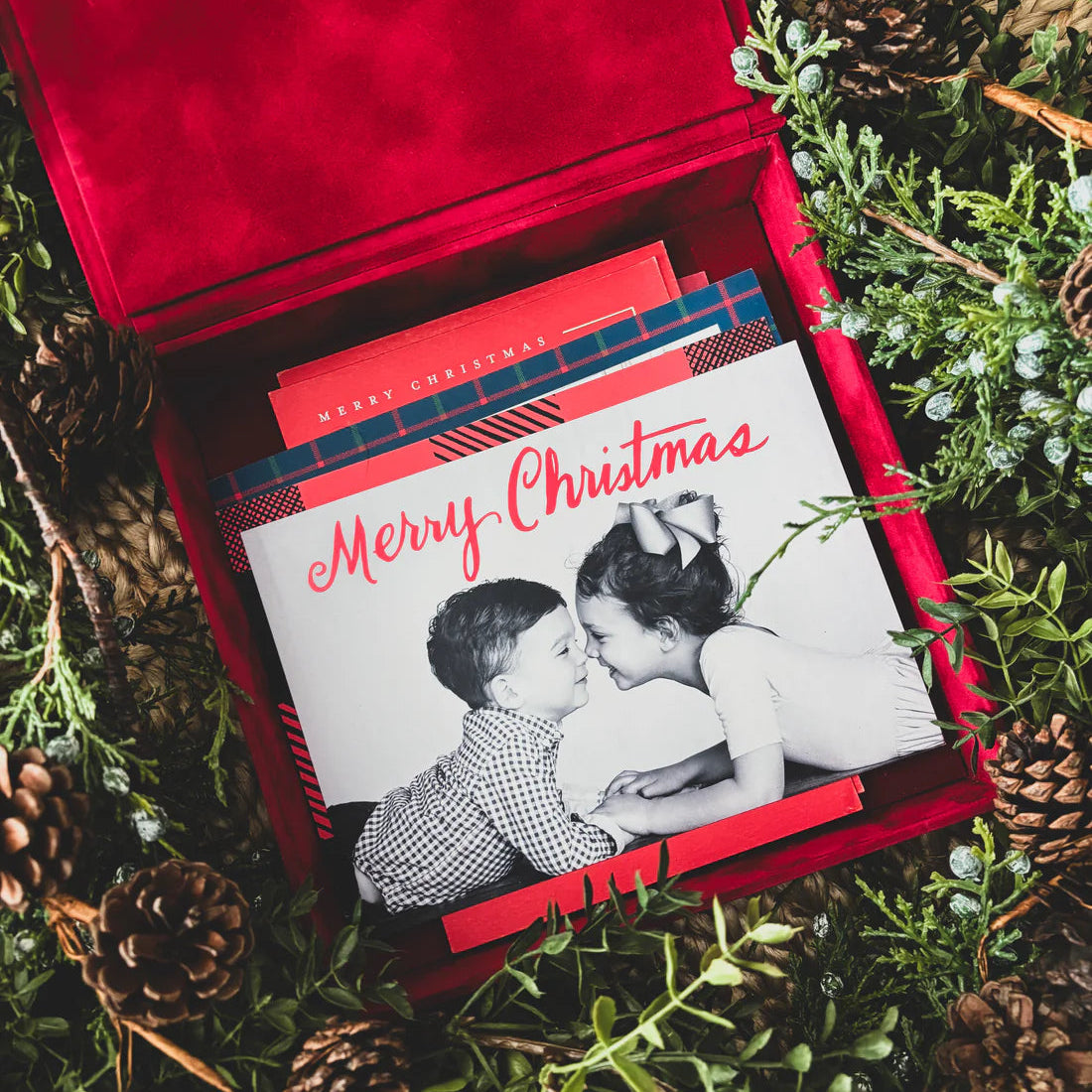 Merry Christmas card with a photo of two people in a red box surrounded by greenery