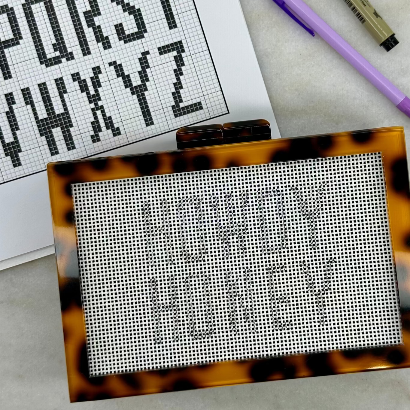Tortoiseshell cross-stitching frame with cross-stitch pattern on a light surface.