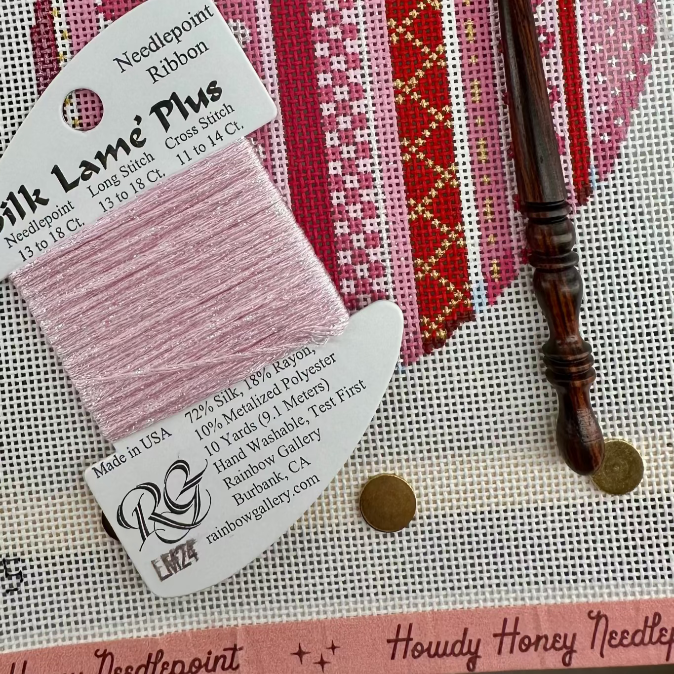 Needlepoint ribbon with a needle and tapestry needle on a textured surface