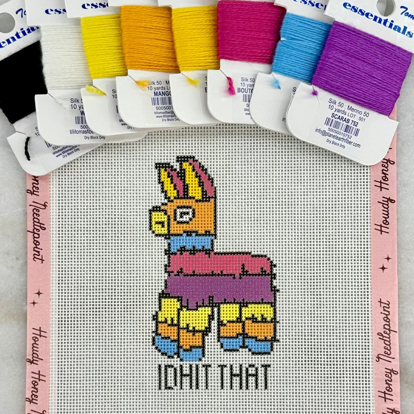 Cross-stitch kit with llama design and colorful threads on a gray background