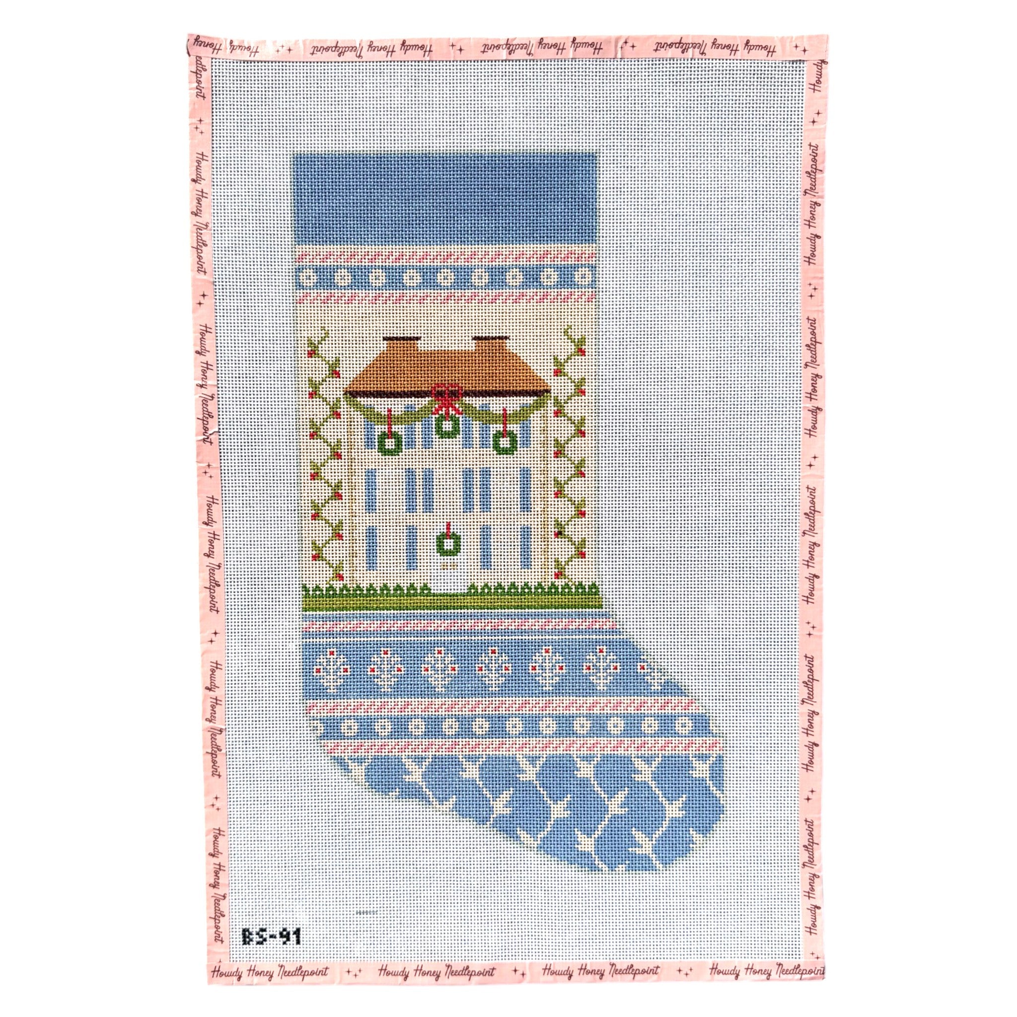 A needlepoint canvas featuring a Christmas stocking design. The stocking has a light blue upper section with a house motif, a green and red wreath, and a light blue lower section with white snowflake patterns.