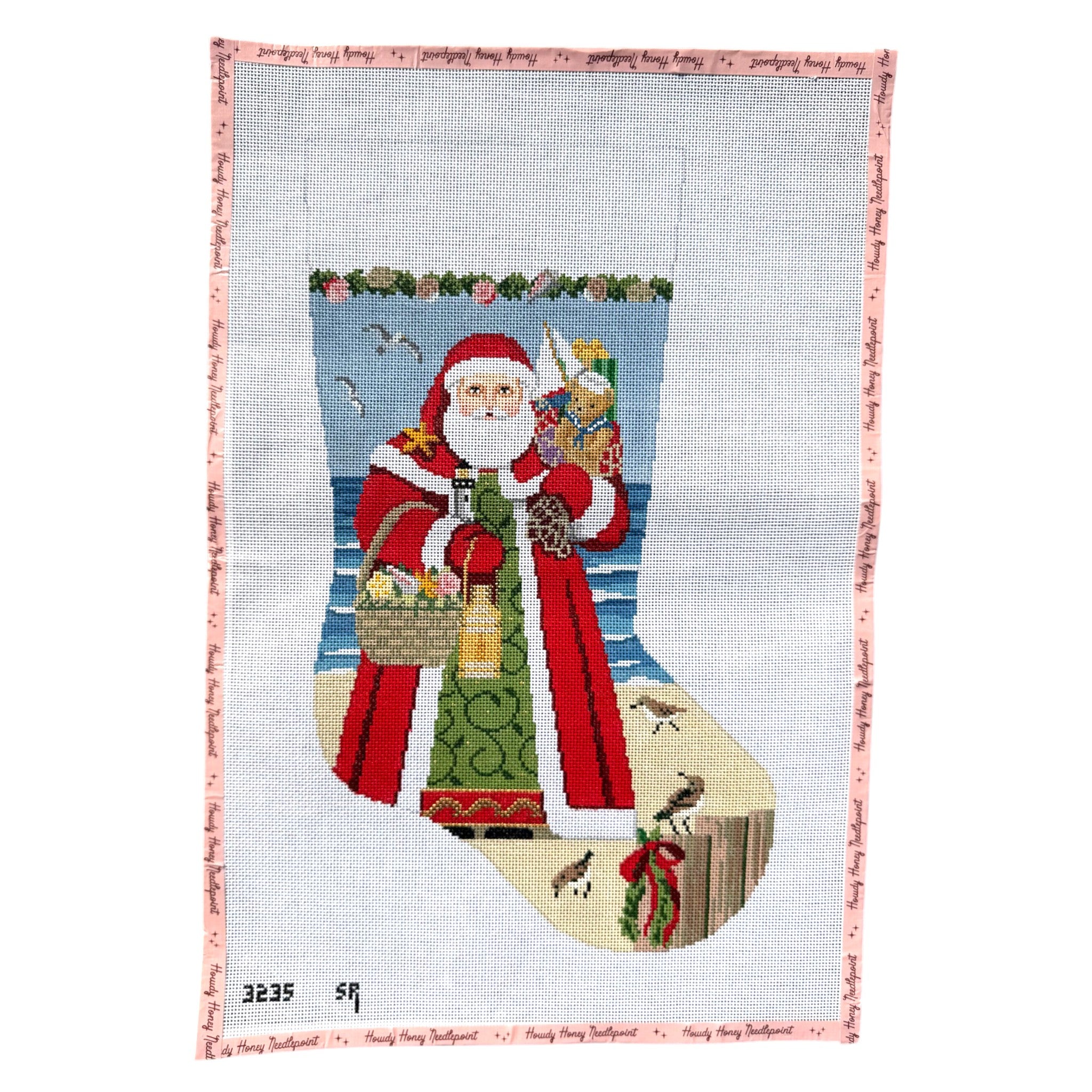 A Christmas-themed needlepoint canvas featuring Santa Claus standing on a beach inside a large stocking, with a pink patterned border and small black numbers '3235 59' in the lower left corner.
