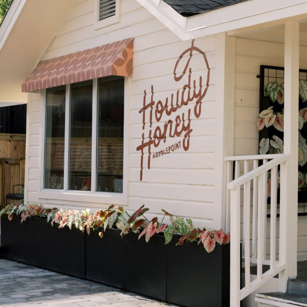 A small white cottage-style building with a porch and black planter boxes along the front, featuring a large script sign reading 'Houdi Honey' on the exterior wall.