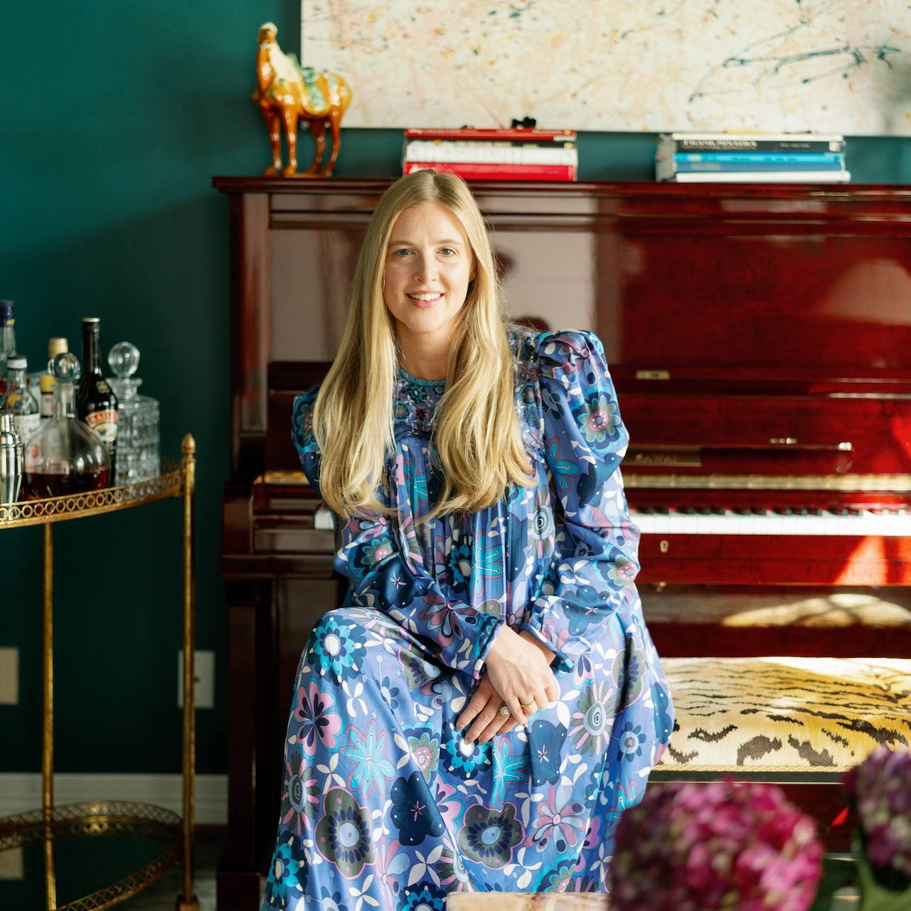 Woman in a blue floral dress sitting in front of a piano in a room with decorative elements.
