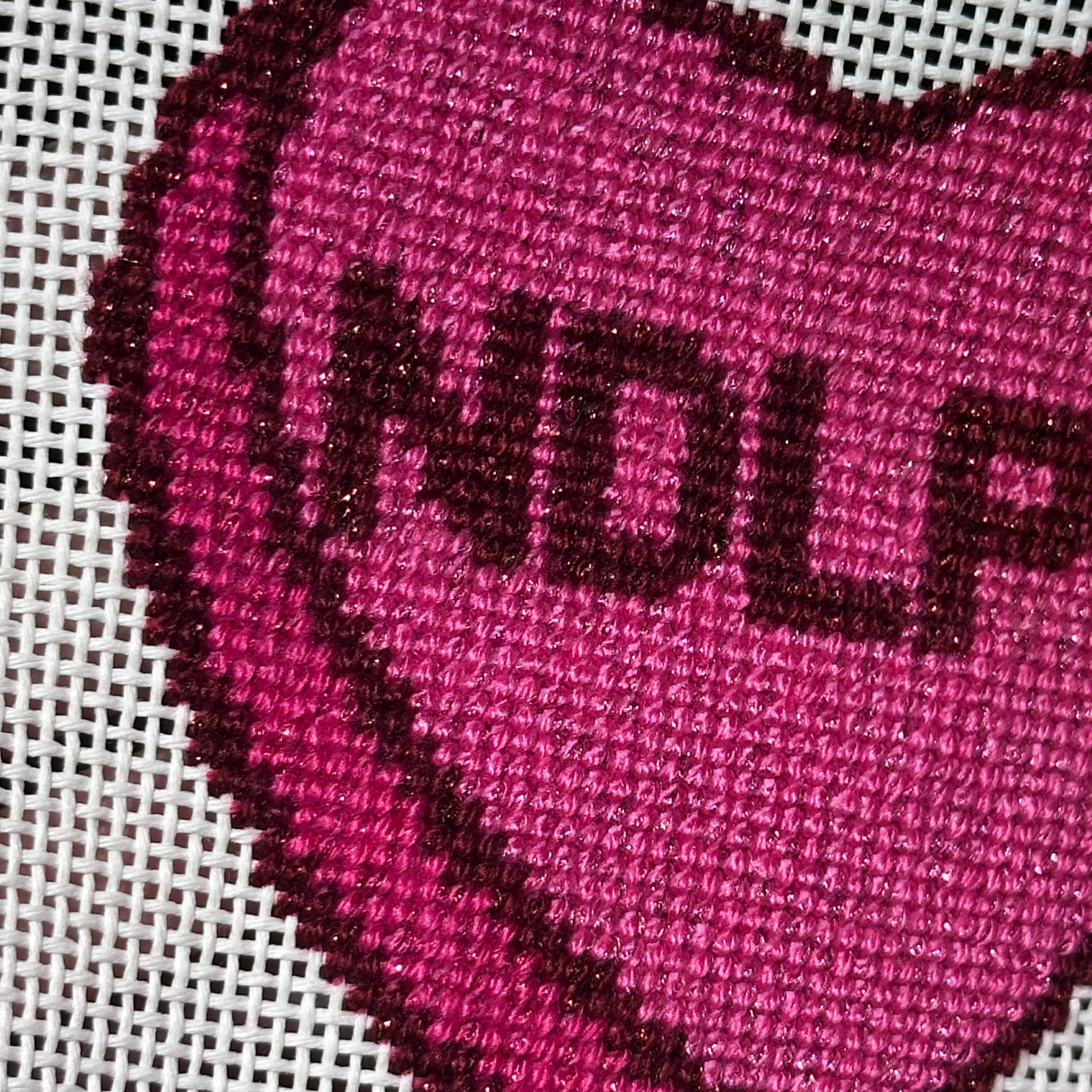 Heart-shaped embroidered design with 'NDL' on a grid background