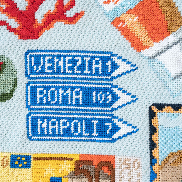 Cross-stitched design with Italian city names and landmarks on a light blue background