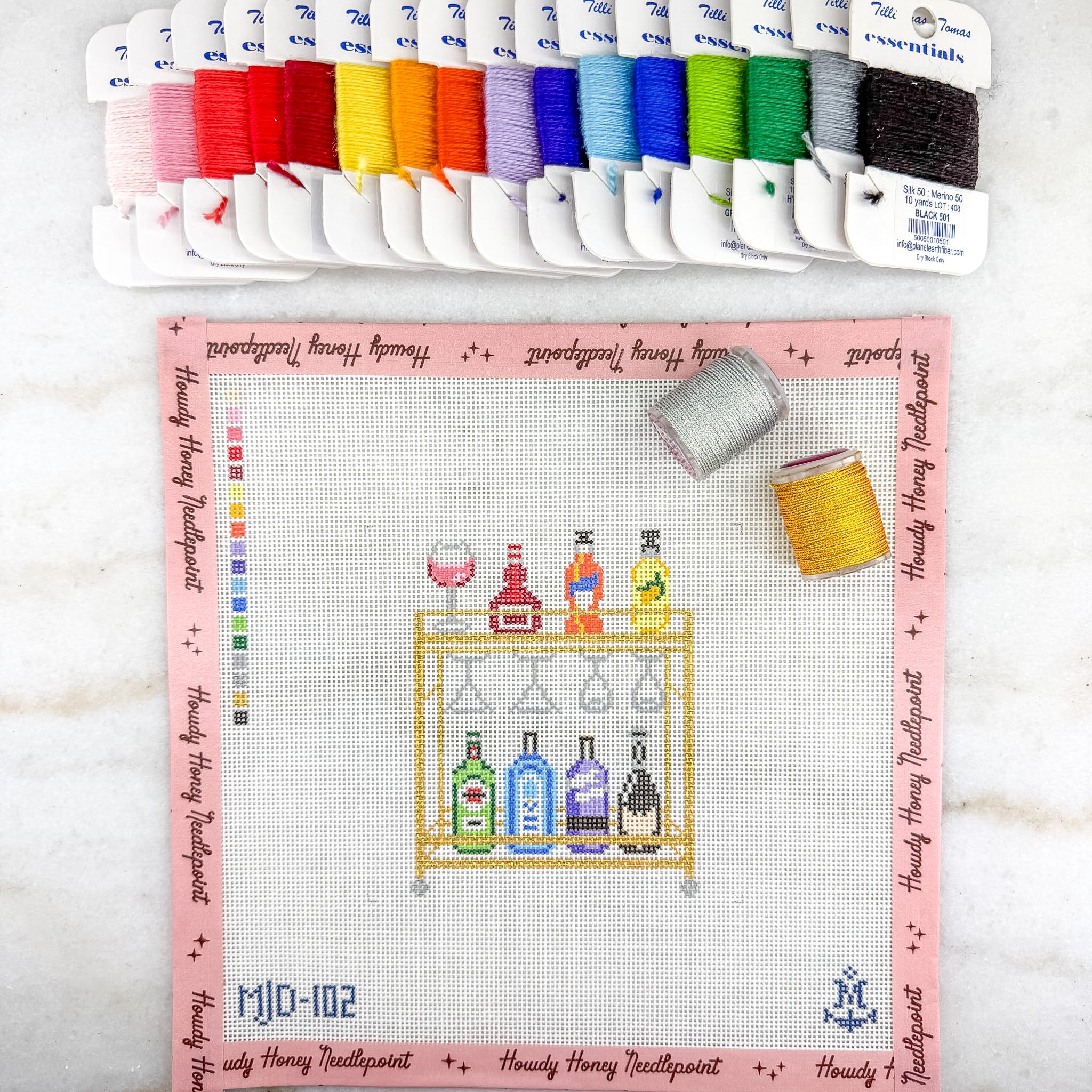 Cross-stitch kit with a bar-themed design and colorful threads on a white background