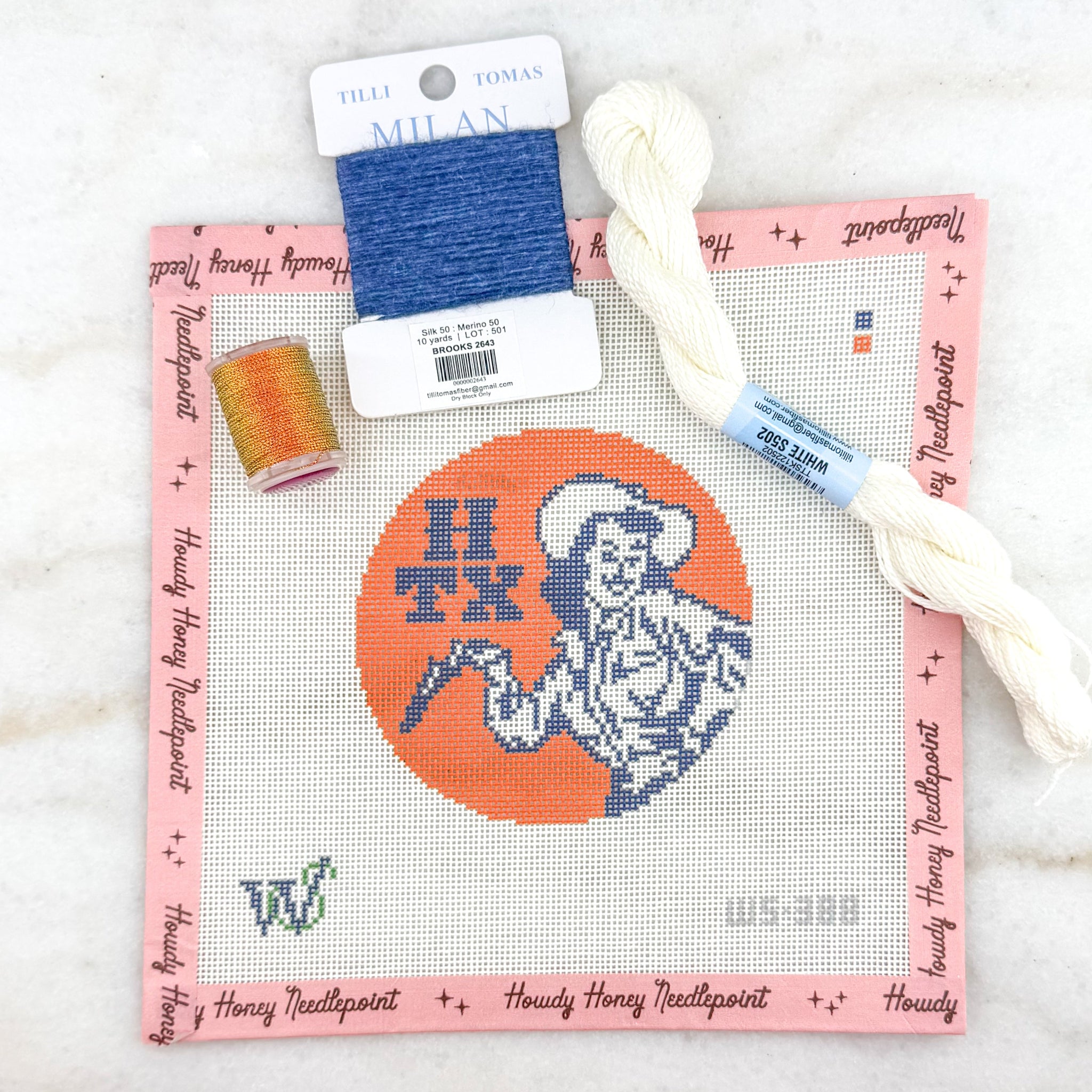Cross-stitch kit with thread and needle on a white marble surface