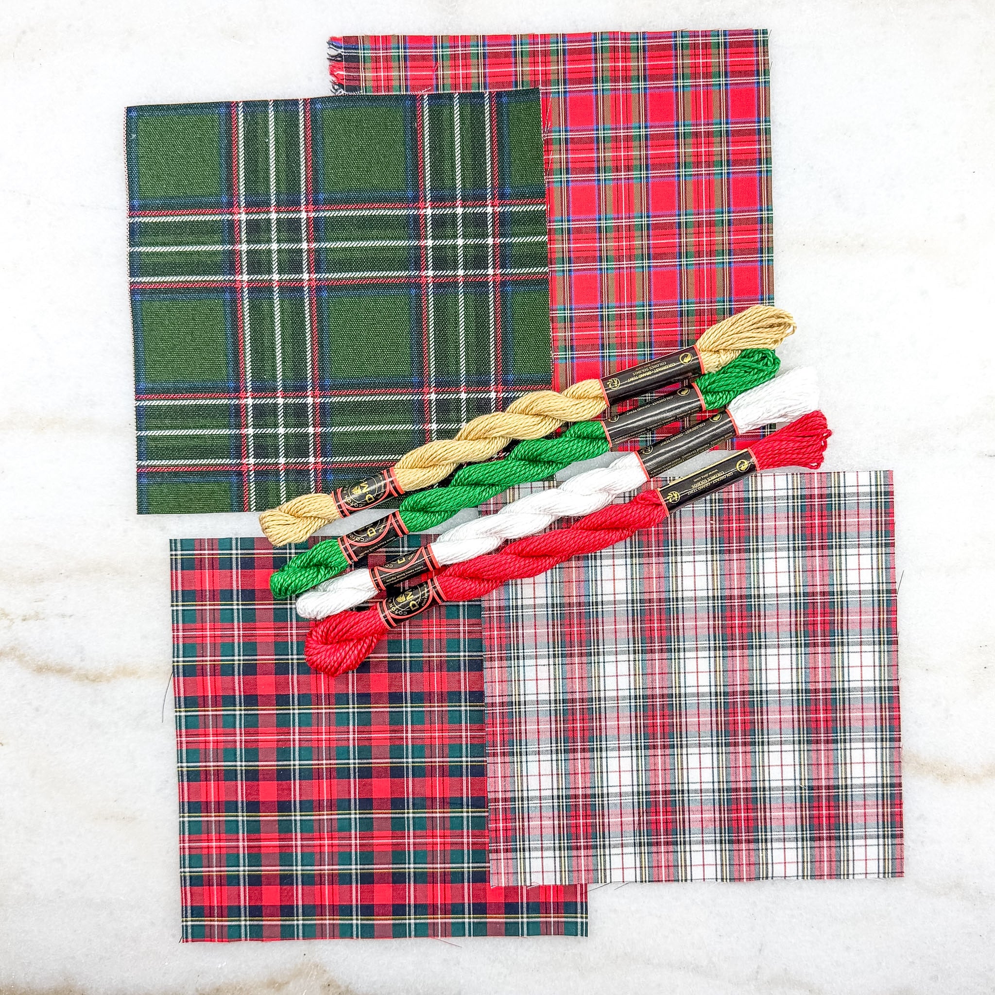 Plaid fabric samples with embroidery floss on a white background