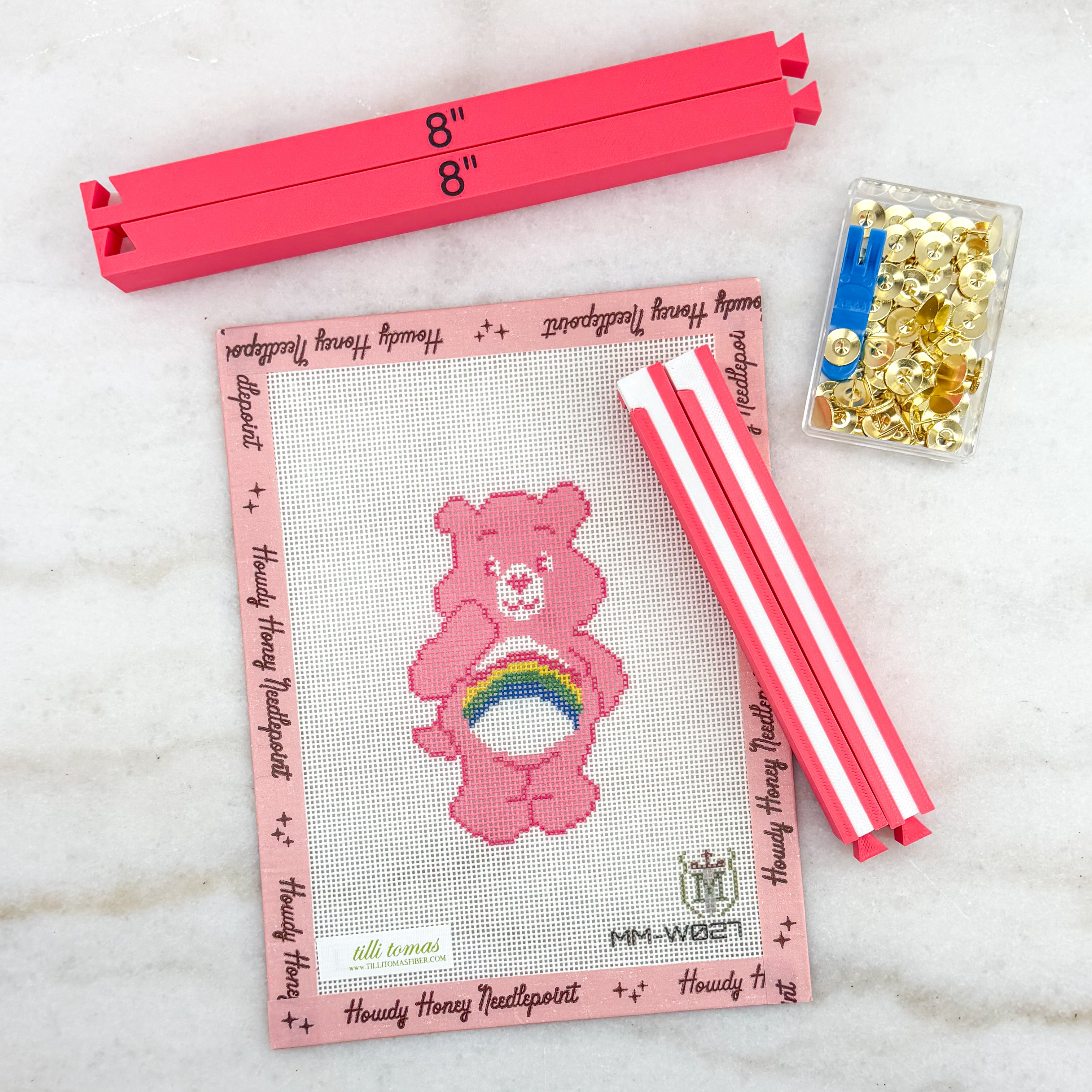 Cross-stitch kit with pink bear design, measuring ruler, and thread on a marble surface