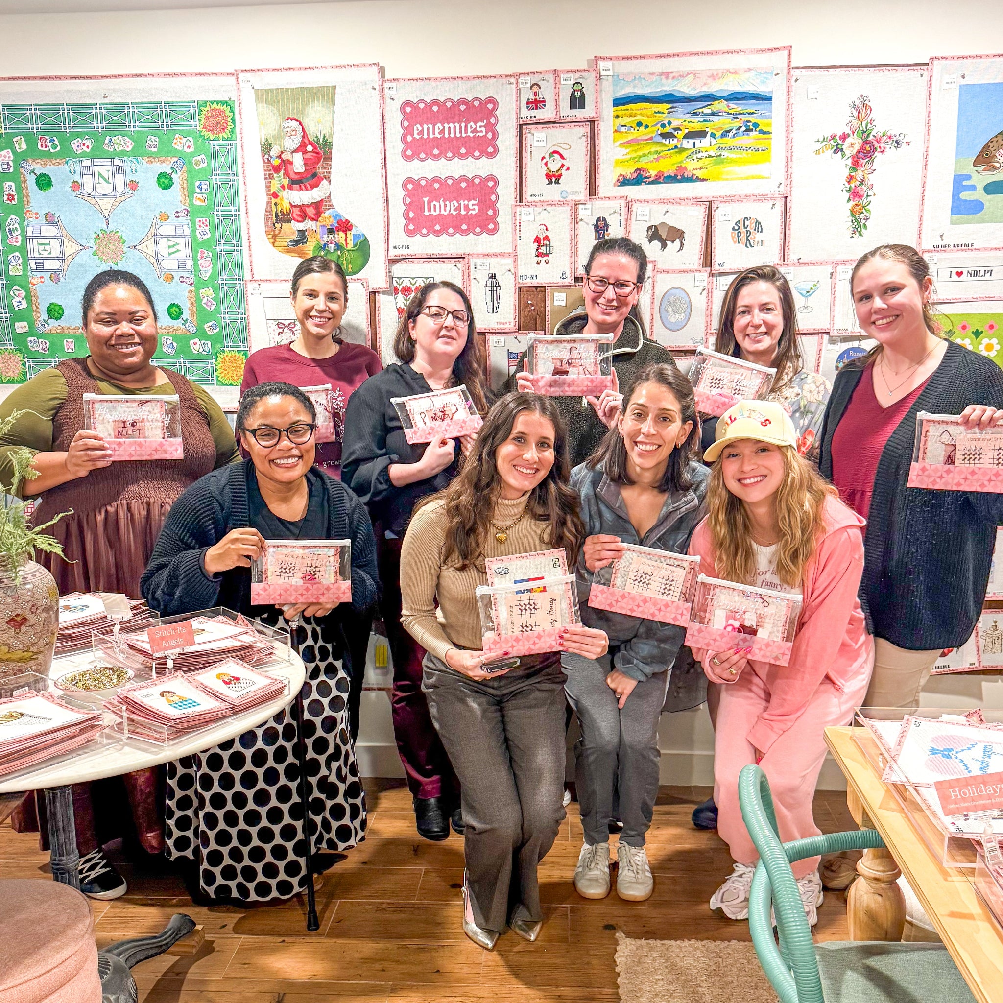 Group of ladies in front of canvas wall holding needlepoint kits.