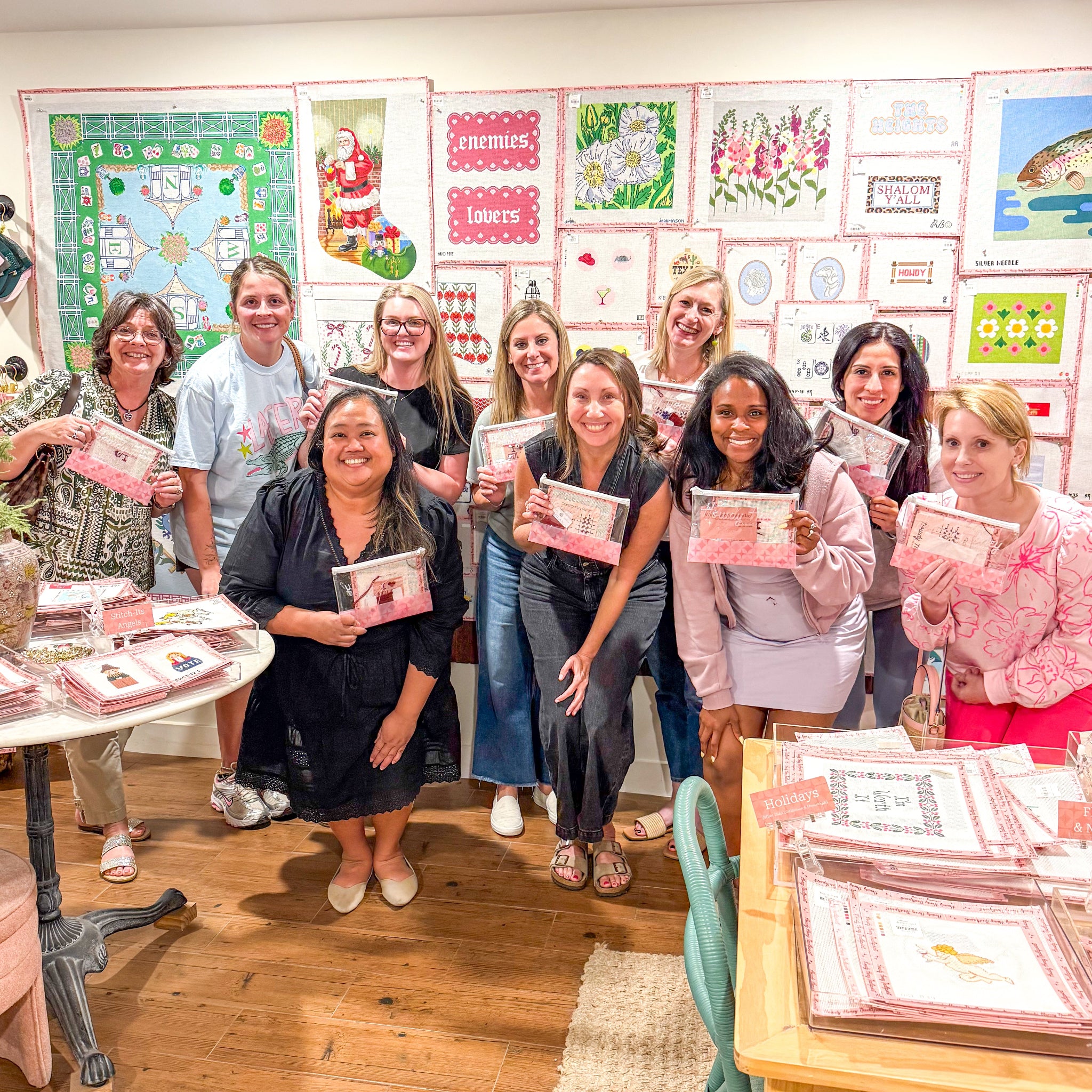 Group of ladies in front of canvas wall holding needlepoint kits.