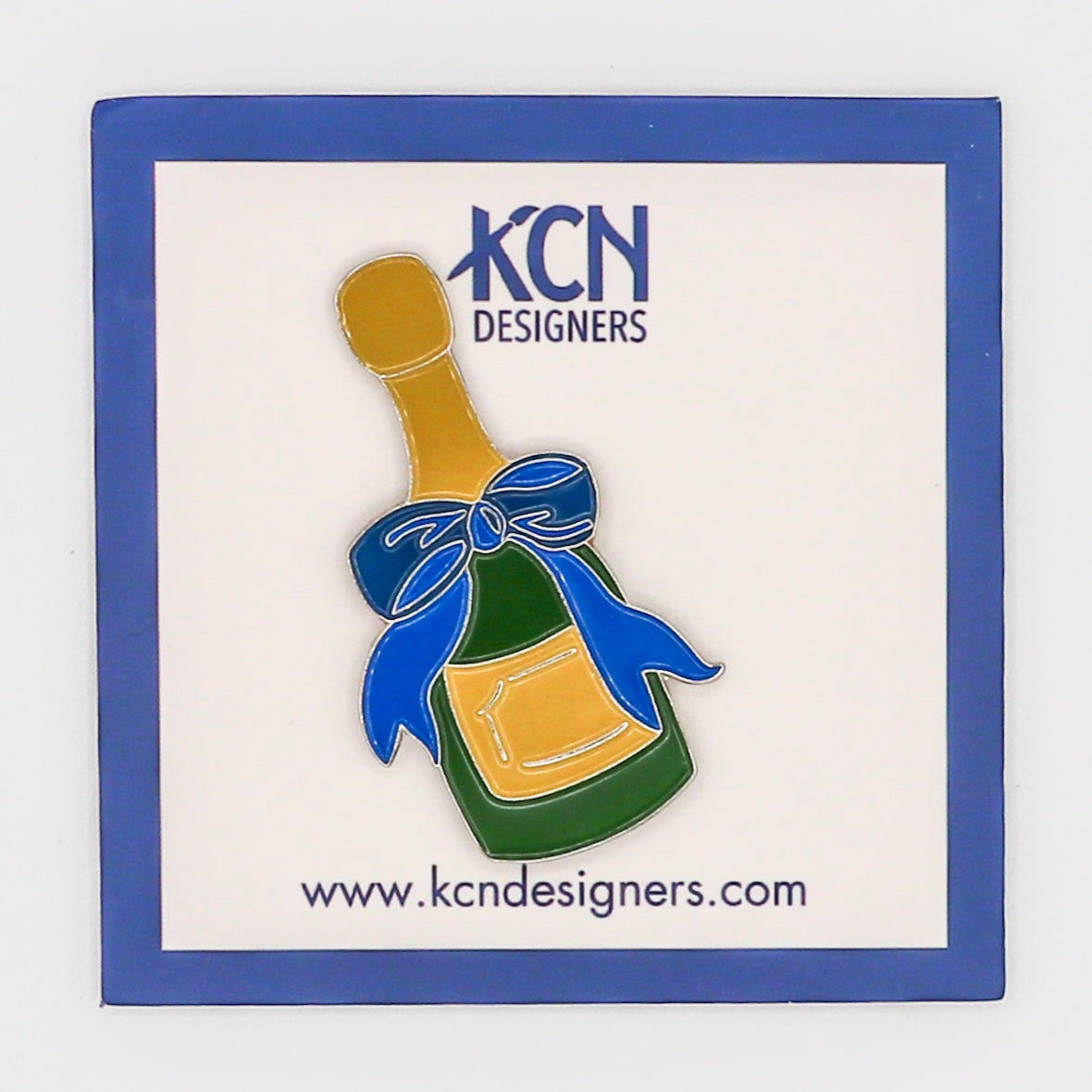 A needle minder with a design resembling a queen wearing a crown, placed in a clear plastic packaging with a purple border and a label with 'KCN DESIGNERS' and a website address.
