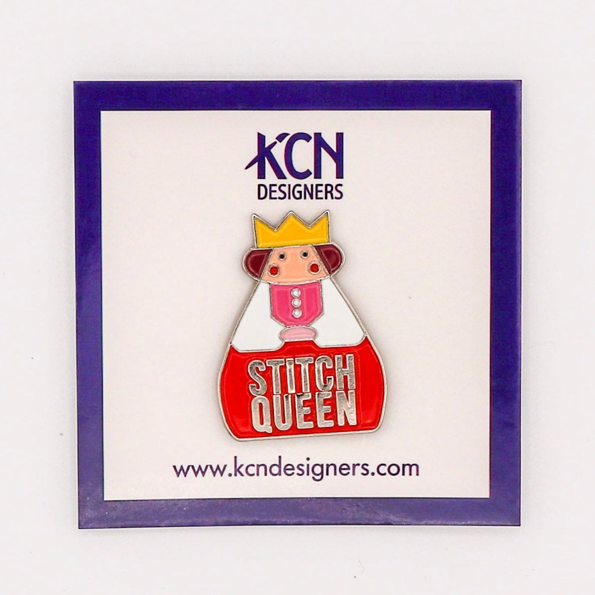 A needle minder with a design resembling a queen wearing a crown, placed in a clear plastic packaging with a purple border and a label with 'KCN DESIGNERS' and a website address.