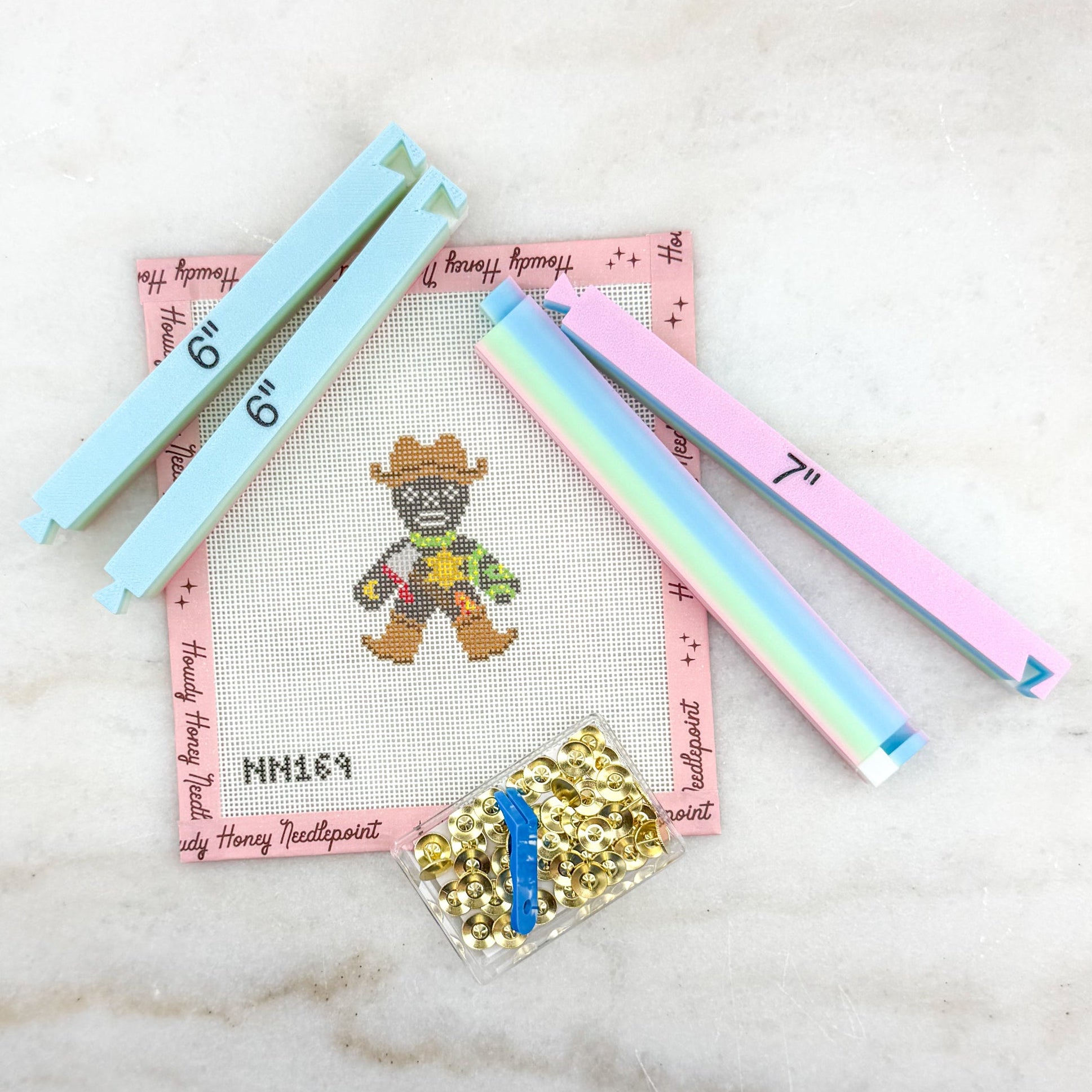 Cross-stitch kit with colorful floss and a small container of gold beads on a marble surface.