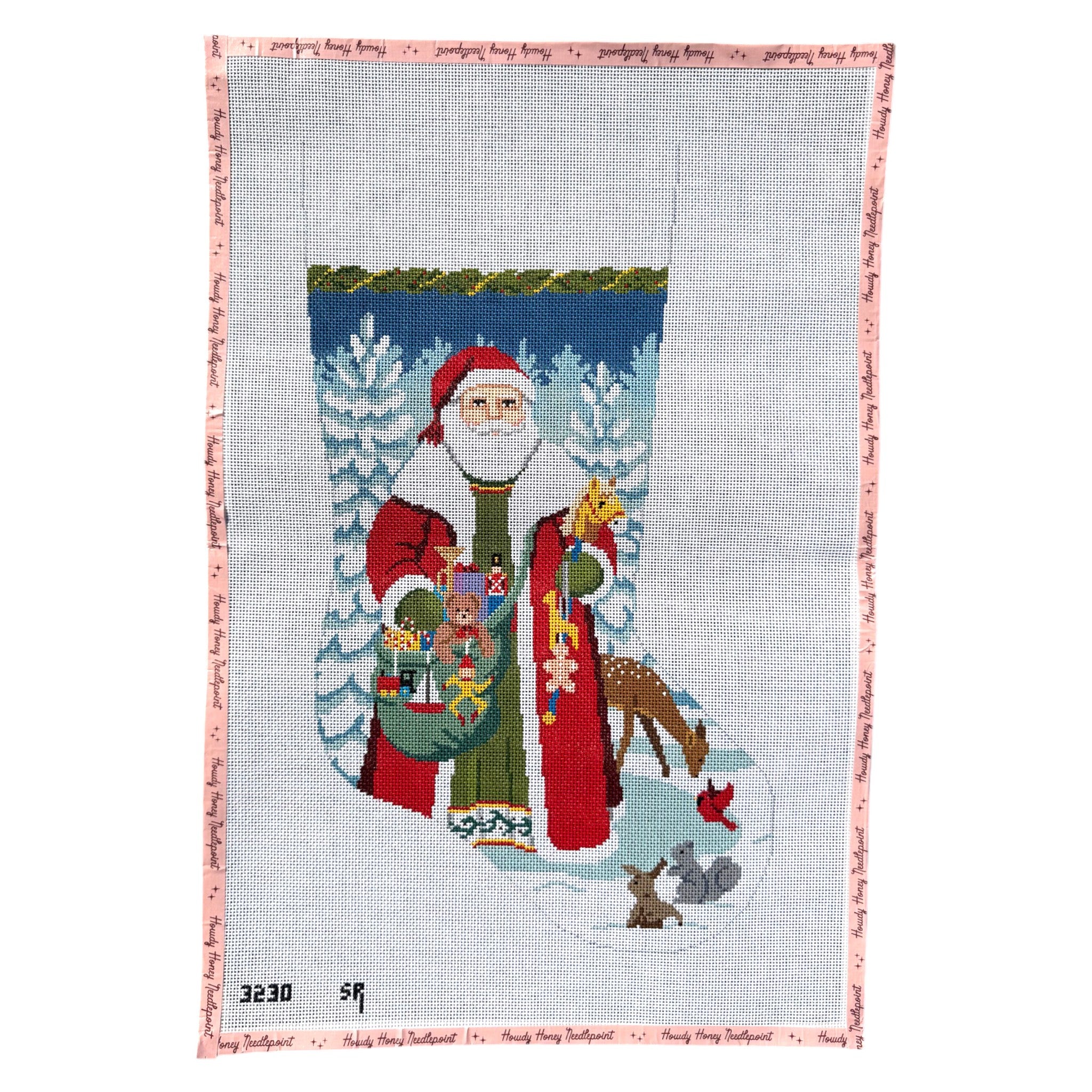 A needlepoint canvas featuring Santa Claus standing in a snowy landscape with a stocking, reindeer, and trees, bordered by a pink and white patterned edge.