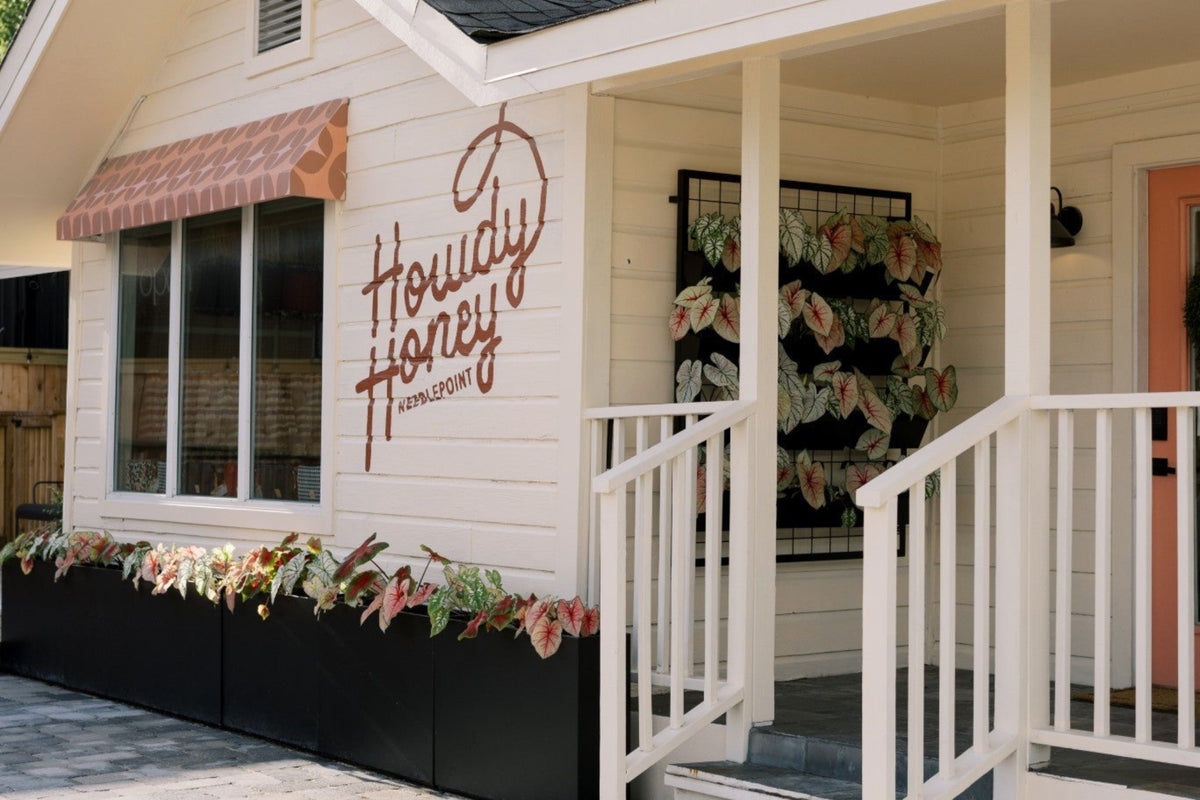 A small white cottage-style building with a porch and black planter boxes along the front, featuring a large script sign reading 'Houdi Honey' on the exterior wall.